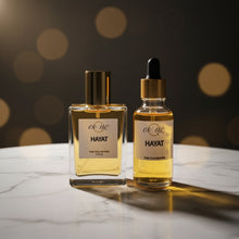 Load image into Gallery viewer, Two bottles - body oil and  Hayat perfume bottles on a windowsill with a cityscape background.